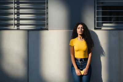 Portrait of young woman standing against wall