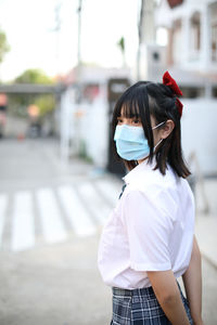 Woman wearing mask looking away standing on street in city