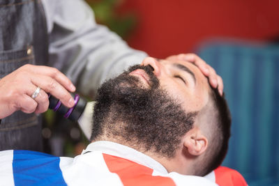 Midsection of barber shaving male customer hair in salon