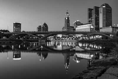 Bridge over river by buildings against sky at night