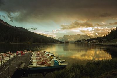 Boats moored at lake misurina by mountains against cloudy sky during sunset