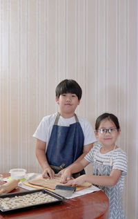 Portrait of siblings preparing cookies on table at home