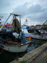 Fishing boats moored at harbor against sky