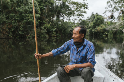 Senior guarani man sitting in canoe at napo river, ecuador