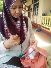Mature woman stitching fabric while sitting against house