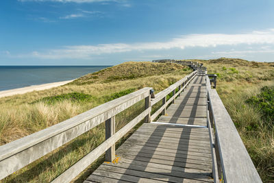 Footbridge on field sea against sky