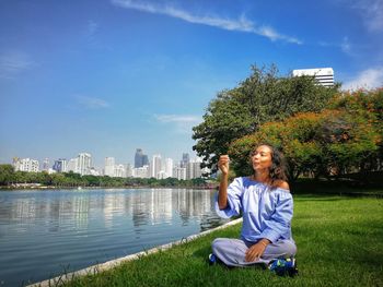 Portrait of smiling young woman sitting by plants against sky