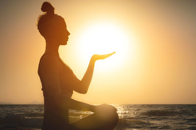 Portrait of a young woman in the form of a silhouette and hands holding the sun. sunset over the sea