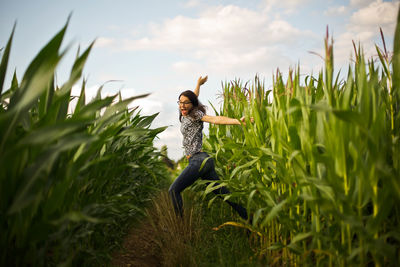 Surprised young woman amidst plants against sky on field