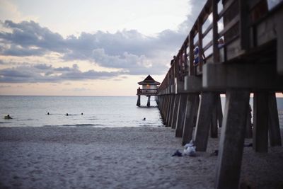 Pier at beach against sky during sunset