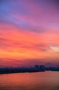 Sea by buildings against sky at sunset