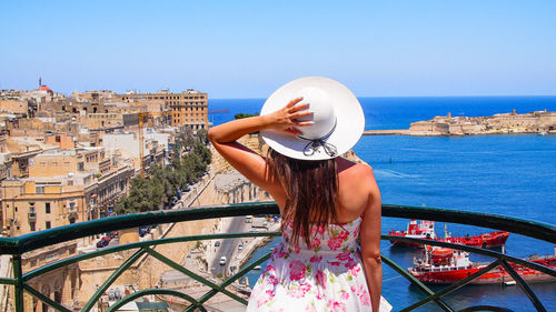 Woman looking at sea by city against clear sky