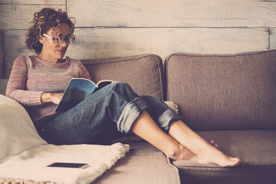 Young woman reading book while relaxing on sofa at home