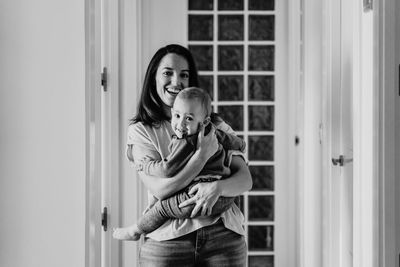 Smiling mother holding daughter at entrance of home