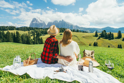 Rear view of couple sitting on mountain against sky