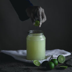 Cropped hand squeezing lime in juice against black background