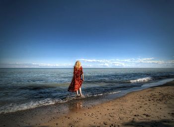 Woman standing at beach against blue sky