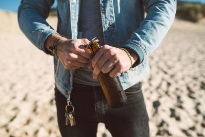 Midsection of man opening bottle on beach