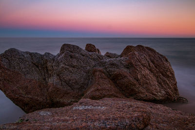 Rock formation on shore against sky during sunset