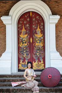 Full length portrait of girl sitting by door of temple