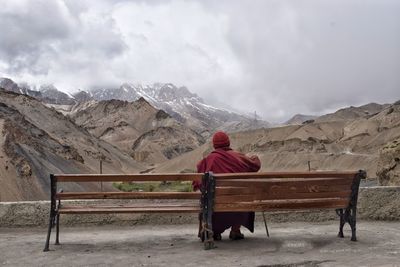 Rear view of man sitting on bench against mountain