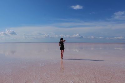 Rear view of woman standing on salt flat against blue sky