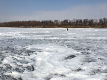 Person in frozen lake against sky during winter