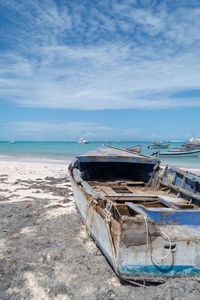 Abandoned boat moored on beach against sky