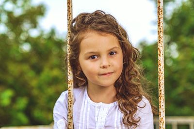 Close-up portrait of girl on swing against trees