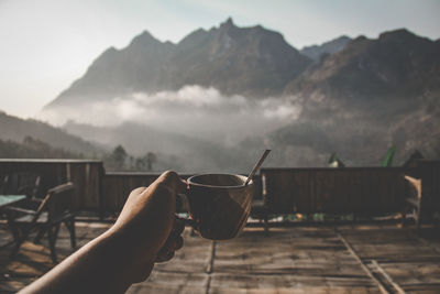 Person holding drink against mountain range