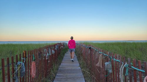 Rear view of person walking on footpath amidst grass against sky