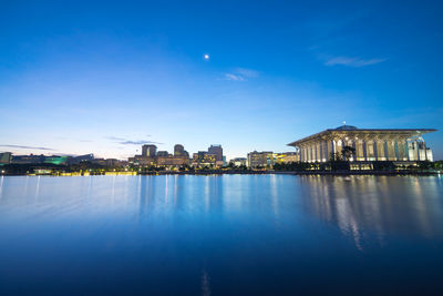 Illuminated tuanku mizan zainal abidin mosque by lake against sky at sunset