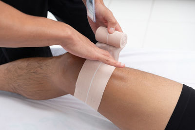Close-up of healthcare worker wrapping bandage on man knee