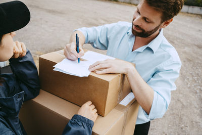 High angle view of man doing paperwork while receiving package from delivery person