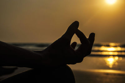 Cropped image of woman practicing lotus position at beach during sunset