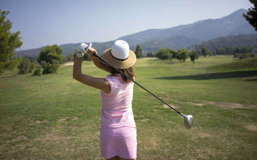 Rear view of woman wearing hat playing golf on field