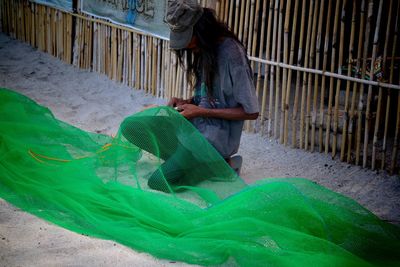 Man working on green net against fence at beach