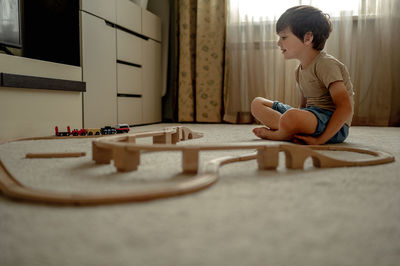 The boy is playing by train at home. the child is building a railway from a wooden construction set