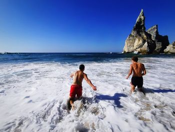 Full length of shirtless man on beach against clear sky