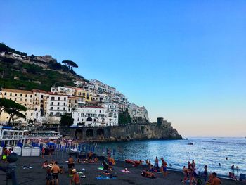 People enjoying at beach by city against clear sky