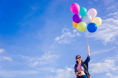 Low angle view of woman holding colorful helium balloons against sky