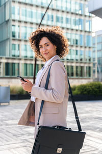 Portrait of young woman using mobile phone while standing in city