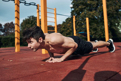 Young shirtless man bodybuilder doing push-ups on a red rubber ground during his workout