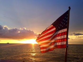 Flag by sea against sky during sunset