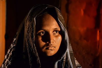 Portrait of young woman standing against black background