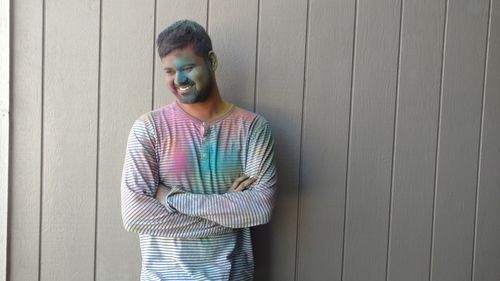 Smiling young man with colorful powder paint looking away while standing against wall