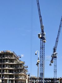 Low angle view of cranes against blue sky