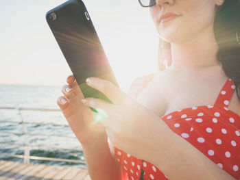 Midsection of woman using mobile phone by sea during sunny day