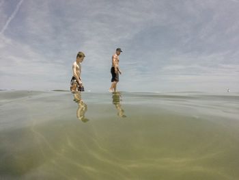 Water level of shirtless father and son in sea against sky