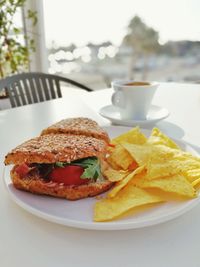Close-up of fresh sandwich and tortilla chips served in plate with coffee on table